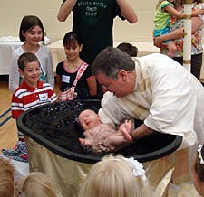 Surrounded by her family, Clare Morgan is baptized by Father Brad Schoeberle, CSP, in the gymnasium of the Allendale Christian School, one of the temporary places of worship for St. Luke University Parish in Allendale, Mich.