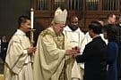 Rev. Mr. Dat Q. Tran, CSP, smiles as Bishop Francisco Gonzalez Valer, SF, accepts the gifts of bread and wine from Rev. Mr. Tran's parents.
