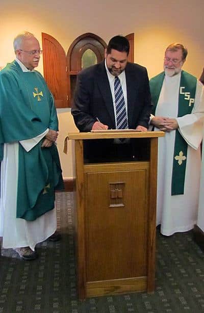 Ryan Casey, CSP, signs the contract in which he promises to live by the Paulist constitution for the next 12 months after making  his first promise with the Paulist Fathers. Paulist President Father Michael McGarry (left) and Novice Director Father Richard Colgan, CSP (right), look on.