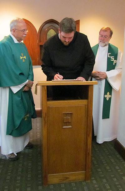 Stuart Wilson-Smith, CSP, signs the contract in which he promises to live by the Paulist constitution for the next 12 months after making  his first promise with the Paulist Fathers. Paulist President Father Michael McGarry (left) and Novice Director Father Richard Colgan, CSP (right), look on.