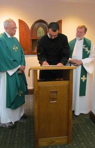 Matthew Berrios, CSP, signs the contract in which he promises to live by the Paulist constitution for the next 12 months after making  his first promise with the Paulist Fathers. Paulist President Father Michael McGarry (left) and Novice Director Father Richard Colgan, CSP (right), look on.