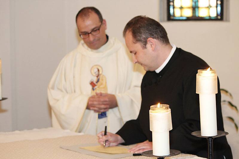Daniel Arthur, CSP, signs the book listing him as a member of the Paulist community after making his first promise as Father Eric Andrews, president of the Paulist Fathers, looks on.